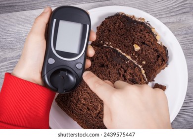 Hand of child holding glucose meter, sweet chocolate cake. Measuring and checking sugar level during diabetes - Powered by Shutterstock