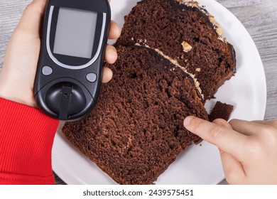 Hand of child holding glucose meter, sweet chocolate cake. Measuring and checking sugar level during diabetes - Powered by Shutterstock