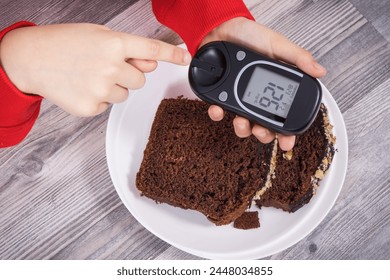 Hand of child holding glucose meter with result of measurement sugar level, sweet chocolate cake. Nutrition during diabetes concept - Powered by Shutterstock