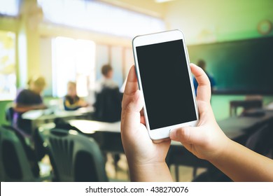 Hand Of Child Holding Mobile Phone With Blur Student In Classroom Background