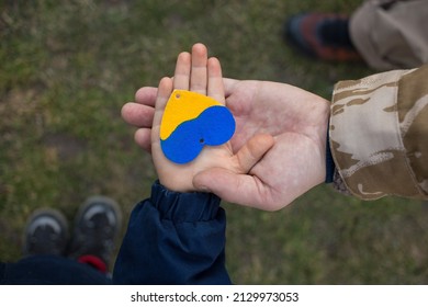 hand of a child in the hand of a man in camouflage with a yellow and blue heart. Family, patriotism, unity, support. Russia's invasion of Ukraine, a request for help to the world community - Shutterstock ID 2129973053