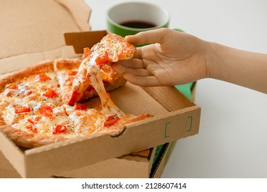In the hand of a child, a piece of hot pizza with which cheese stretches against the background of a whole round pizza. The concept of fast delivery, take off, snack, hot snack.