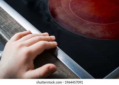 Hand Of A Child Reaches Active Hotplate Of A Kitchen Glass-Ceramic Stove - Prevent Child Hazard Concept