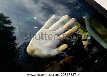 A hand of a child or young woman locked in the car with the reflections of forest trees. Kidnapping, crime and danger theme.