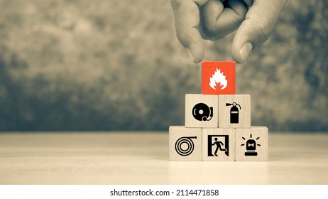 Hand choose wooden block stack with fire icon with door exit with fire extinguisher and emergency prevent protection symbol for safety. - Shutterstock ID 2114471858