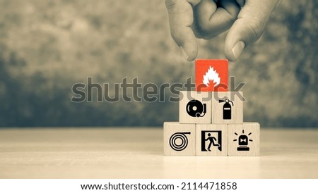 Hand choose wooden block stack with fire icon with door exit with fire extinguisher and emergency prevent protection symbol for safety.