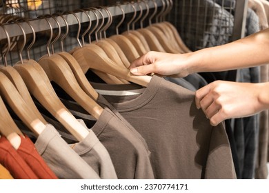 Hand choosing discount t-shirt clothes in store, searching or buying cheap cotton shirt on rack hanger at flea market. Shopping concept.