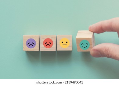 Hand choosing happy smile face wooden block, good feedback rating and positive customer review, mental health assessment, child wellness,world mental health day, think positive, compliment day concept - Shutterstock ID 2139490041