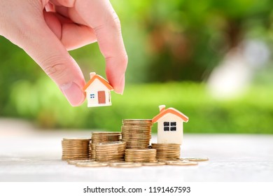 Hand Choosing Mini House Model On Coins Stack. Planning To Buy Property. Choose The Best.