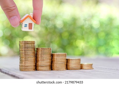 Hand Choosing Mini House Model On Coins Stack. Planning To Buy Property. Choose The Best.	