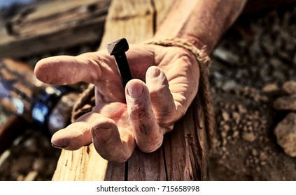 Hand of Christ nailed to the cross with a close up view of a mans hand with an iron nail hammered through onto a wooden cross symbolic of the crucifixion of Christ at Easter