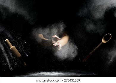 Hand Clap Of Chef With Wooden Rolling Pin And Spoon In The Air With Splash Flour On Black Background