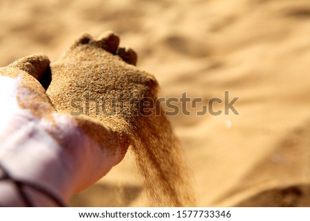 Hand clasping golden sand falling through the finger, with place for text