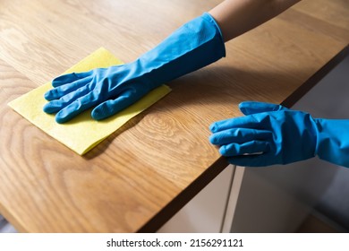 Hand of cleaner wearing blue protective rubber gloves, washing table top or kitchen counter, table top wooden surface, rubbing furniture with rag. Close up shot. Household, cleaning service concept