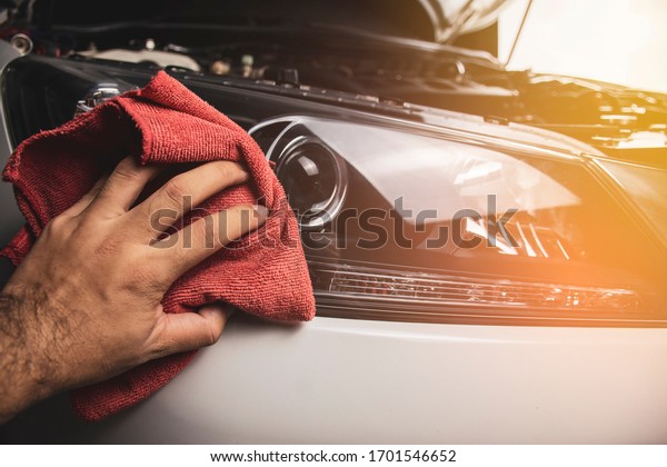 Hand is cleaning
car headlight with a using red microfiber cloth,Automotive
maintenance concept.