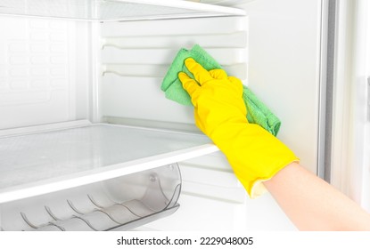 Hand cleaning refrigerator. Person washing refrigerator with rag. Housekeeper wipes shelves of clean refrigerator. Hand in yellow rubber protective glove and green sponge washes - Powered by Shutterstock