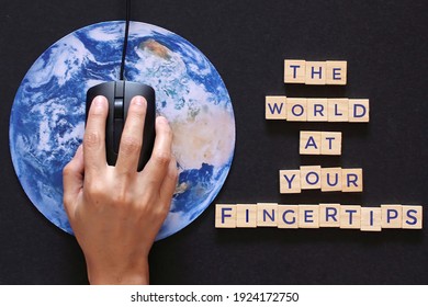 Hand clicking computer mouse on planet earth globe and wooden cube with text THE WORLD AT YOUR FINGERTIPS.