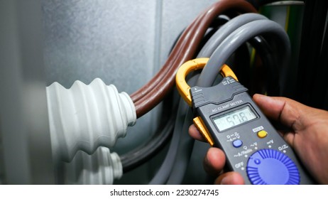 Hand closeup of electrical engineer to use digital ampere meter to measurement electrical current from power cable in feeder cabinet in electricity substation, industrial and energy concept