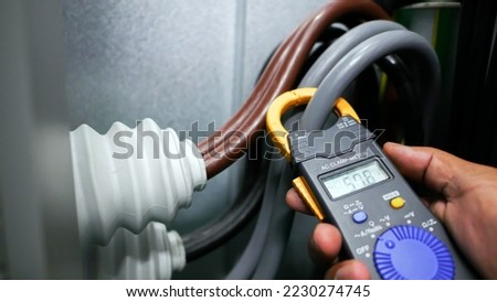 Hand closeup of electrical engineer to use digital ampere meter to measurement electrical current from power cable in feeder cabinet in electricity substation, industrial and energy concept