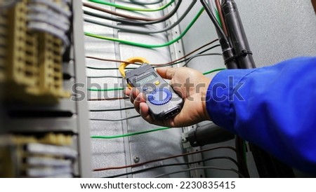 Hand closeup of electrical engineer to use digital ampere meter to measurement electrical current from power cable in feeder cabinet in electricity substation, industrial and energy concept