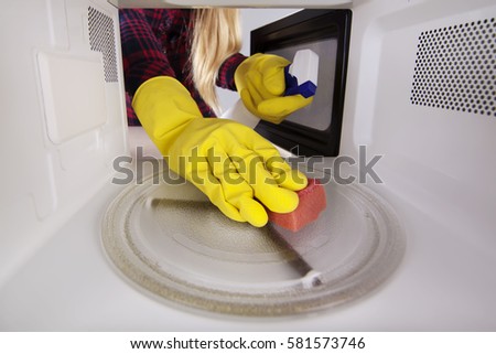 Hand close-up in gloves with sponge wiping inside of microwave. Open oven young woman with spray bottle cleaning