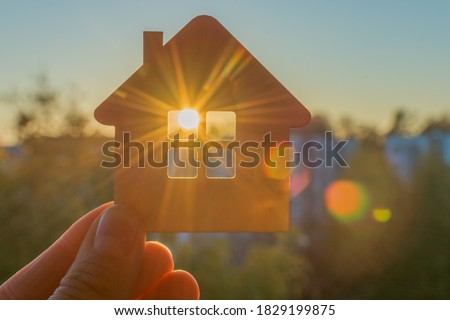 in hand a close-up of a small sketchy wooden house, through the window of which the sun's rays of the setting or rising sun are visible. The idea is to find your own home, hoping for a new day.