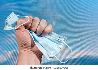 Hand Clutching A Medical Mask Against The Background Of A Mosquito Net. We Quit Quarantine