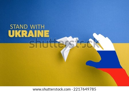 hand with colors of russian flag catches paper dove on yellow and blue background with words stand with Ukraine. terror and annexation