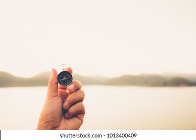 Hand with compass at mountain road at sunset sky - Shutterstock ID 1013400409