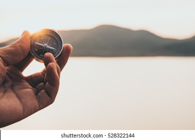 Hand with compass at mountain road at sunset sky  - Shutterstock ID 528322144