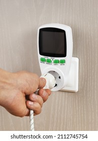 Hand connects plug with wattmeter socket on wall, for measuring electricity costs in device, close-up - Shutterstock ID 2112745754