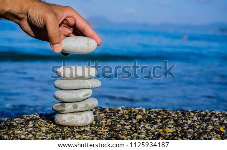 A hand constructs equilibrium on pebbles. Perfect balance of stack of pebbles on the seashore. Concept of balance, harmony and meditation. Helping or supporting someone for growing or going higher.