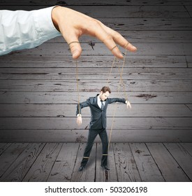 Hand controlling businessman as puppet on wooden background. Control concept