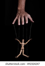 Hand controlling wooden puppet marionette, low key images, on black background