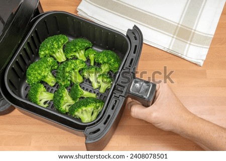 HAND COOKING BROCCOLI FLORETS IN AIR FRYER AT THE KITCHEN. VEGAN FOOD AND KETO DIET CONCEPT. TOP VIEW.
