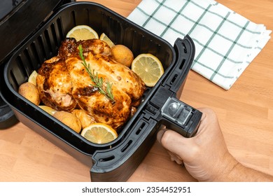 HAND COOKING WHOLE ROASTED CHICKEN WITH GARNISH IN AIR FRYER AT THE KITCHEN. TOP VIEW