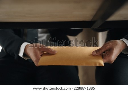 Hand of a corrupt businessman or politician is offering a bribe given in the form of a brown envelope of money to do an illegal business. Corruption and bribery concept.