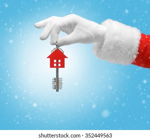 Hand In Costume Santa Claus Is Holding House Keys / Studio Shot Of Man's Hand Holding Keys / Merry Christmas & New Year's Eve Concept / Closeup On Blurred Blue Background.