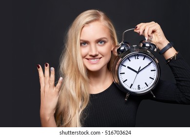 Hand counting - number four. Smiling woman holding big alarm clock showing four fingers, portrait over grey background