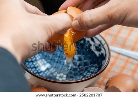 A hand cracking a chicken egg into a bowl, with a black spot visible on the yolk