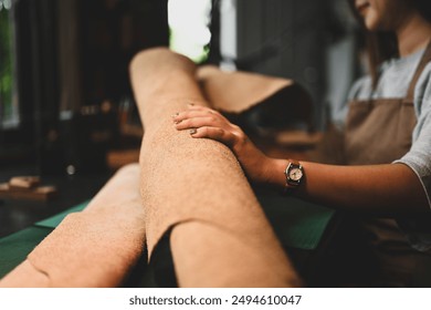 Hand of craftswoman examining a large roll of leather at her workbench surrounded by tools. - Powered by Shutterstock