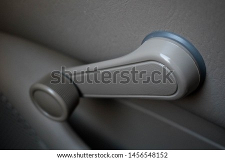 Hand crank, non-electric, manual car window knob in a dove grey color an old vehicle. Changing automobile technology concept.