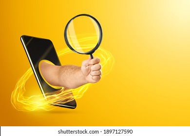 The hand crawling out through the smartphone holds, offers a magnifying glass on a yellow background. Online search concept, instant access to information. Copy space
