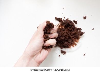 Hand Crushing A Chocolate Muffin In A Fist Against A White Background. Top Down View Of Crumbs And Mess.