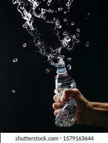 Hand Crushing A Water Plastic Bottle And Drops Spilling Out On Black Background