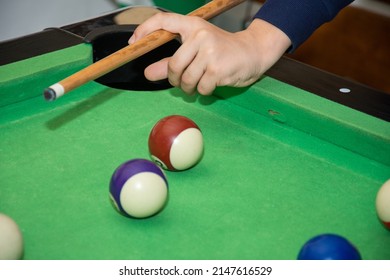 Hand with cue aiming on billiard ball at table