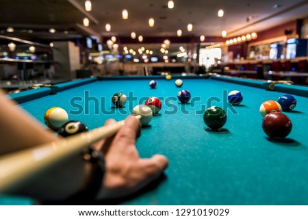 Hand with cue aiming on billiard ball at table