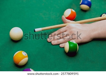 A hand with a cue preparing to strike on a billiard table with balls for eight-ball, close-up of billiard gameplay, background for a billiard or sports bar, hitting the cue ball in billiards.