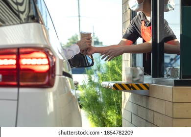 Hand Of Customers In The Car Is Picking Up A Personal Cup Of Coffee From The Salesman  Wearing A Mask To Prevent The Coronavirus Outbreak By Driving Through Or Drive Thru. (Social Distancing)