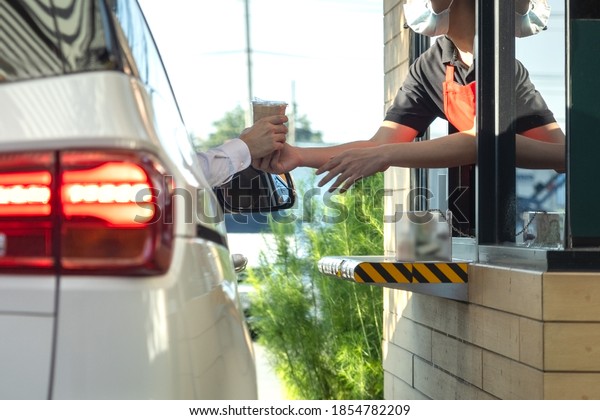 Hand\
of customers in the car is picking up a personal cup of coffee from\
the salesman  wearing a mask to prevent the coronavirus outbreak by\
driving through or drive thru. (Social\
distancing)